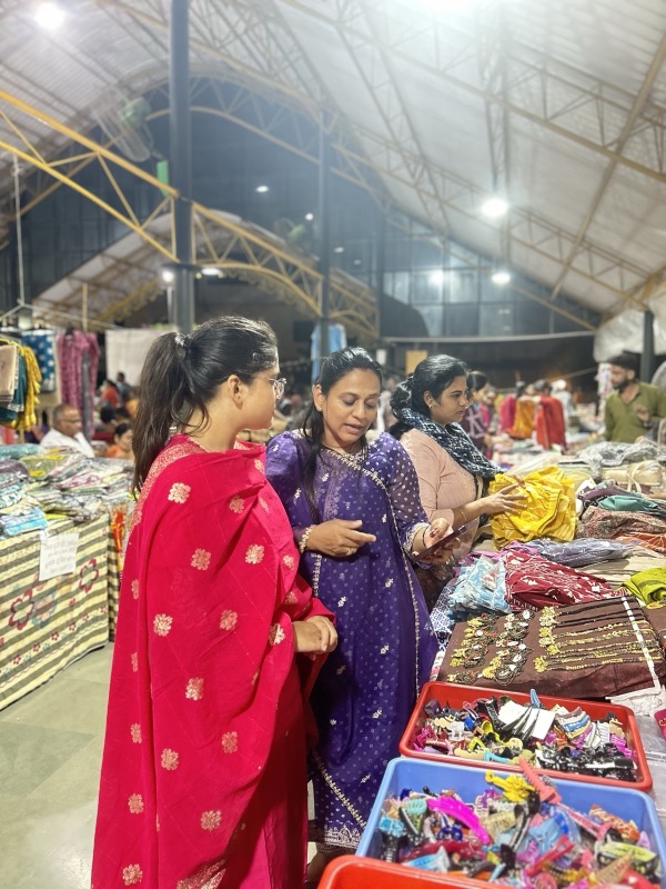 Siddhali Anup Shah browsing handmade goods with women at a local market stall